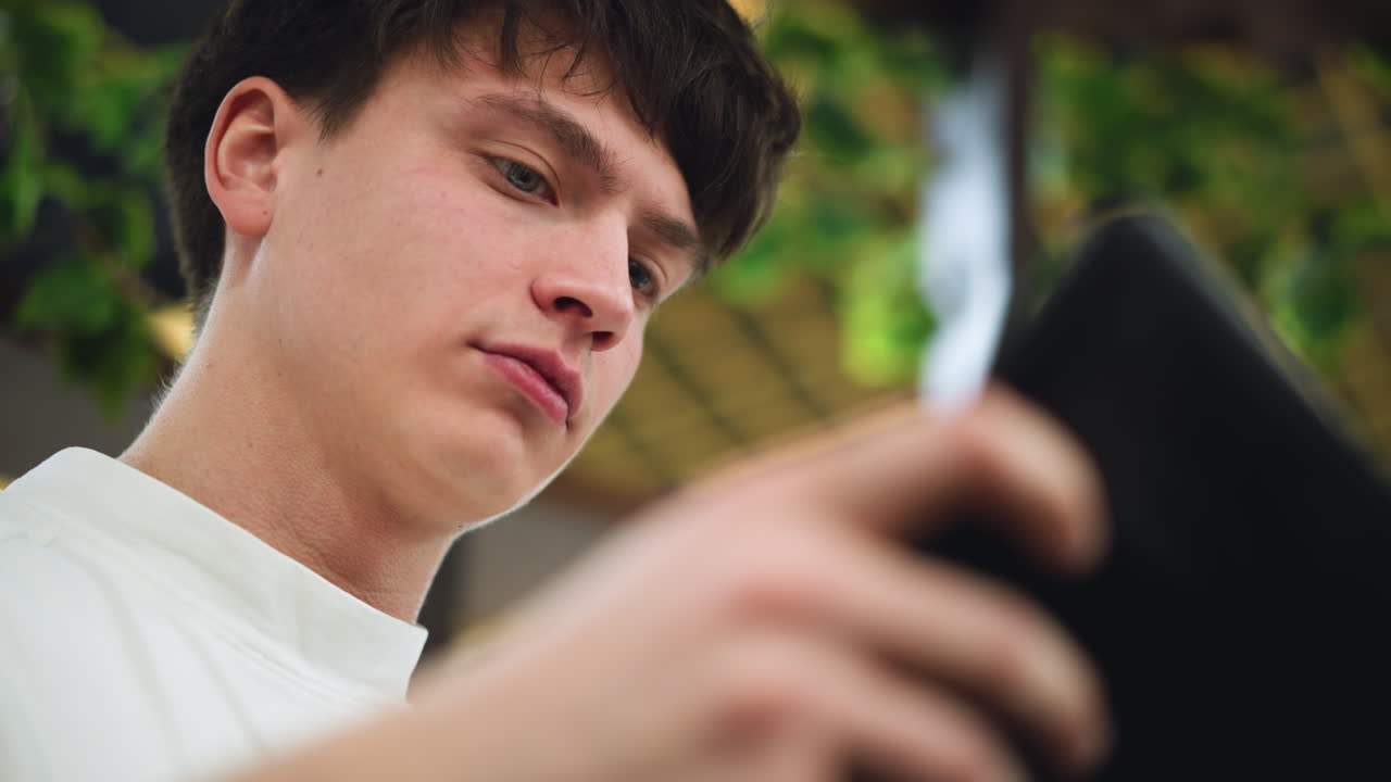 Under angle view white young boy leaning forward eyes fixed on smartphone screen full bushy eyebrow casting shadow on face capturing moment of digital immersion and youthful concentration in room