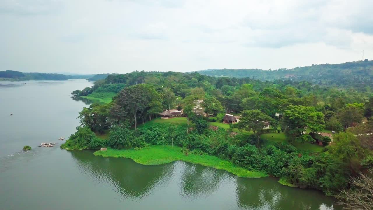 Aerial view of a lodge nestled among lush greenery on the banks of the River Nile in Uganda, Africa, with its reflection shimmering in the tranquil water under a cloudy sky
