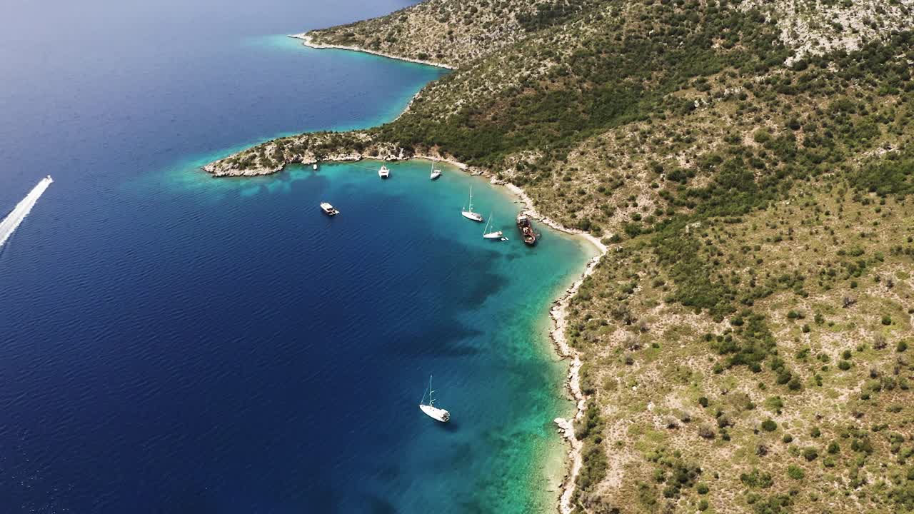 Drone footage. Boats on the island beach, on the left side speed boat crusing beside the shore. Sand beach and rocky uphill.