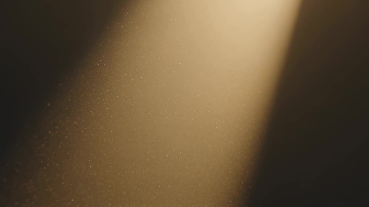 Drifting warm golden beam revealing dust motes swirling slowly in dark studio from gentle breeze