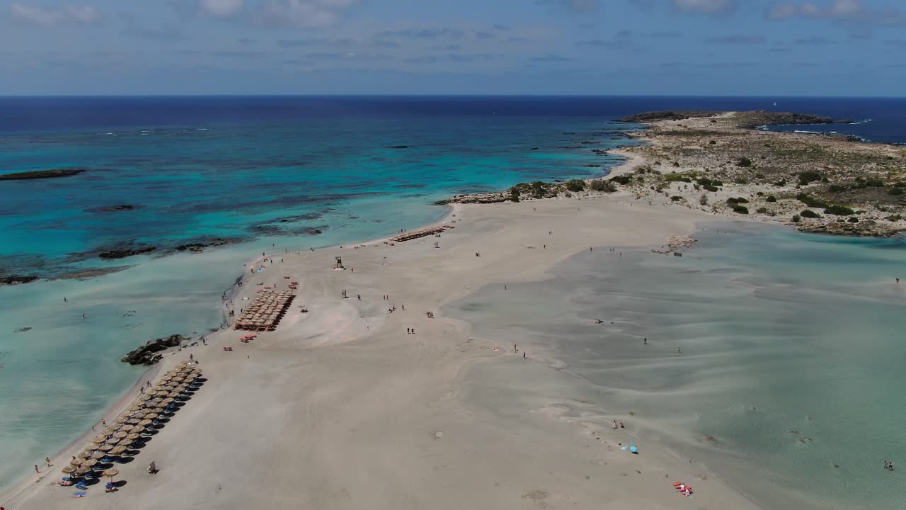 Elafonissi Peninsula in Crete Greece with beach sunshade parasols and bathers enjoying the water, Aerial dolly in shot