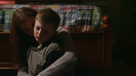 una madre con sus brazos alrededor de su hijo pequeño, que parece triste