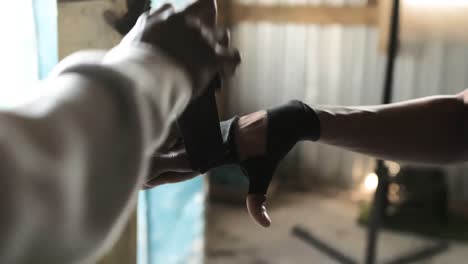 Mid-section-of-Coach-tying-hand-wrap-to-a-Boxer-in-the-gym