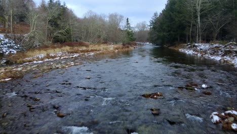 low-drone-footage-of-a-wintry-woodland-stream-with-snow-in-a-forest