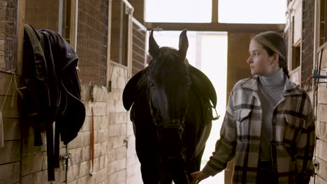 jinete femenino que llega al establo con el caballo negro