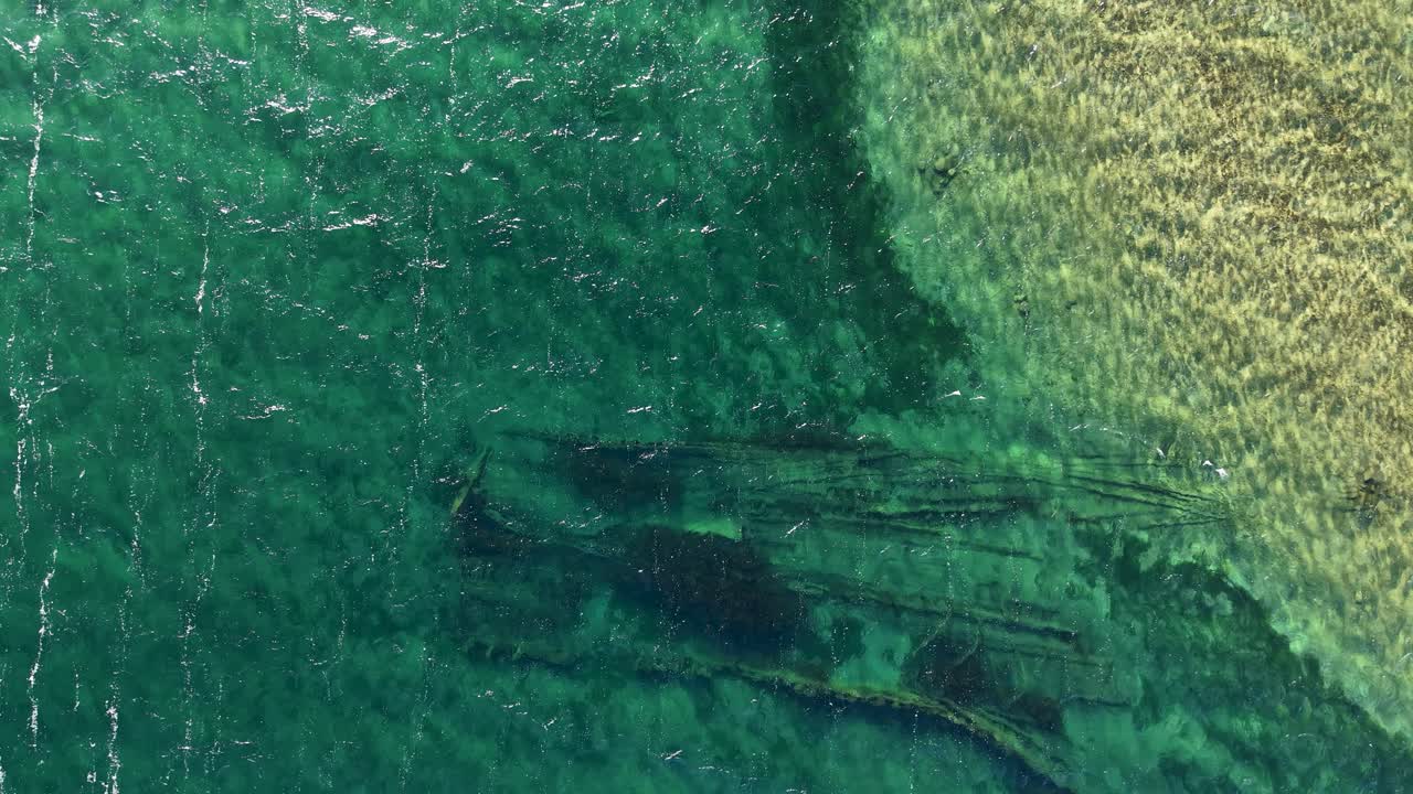 Aerial view of submerged shoreline revealing dark underwater shipwreck and features and clear water gradients