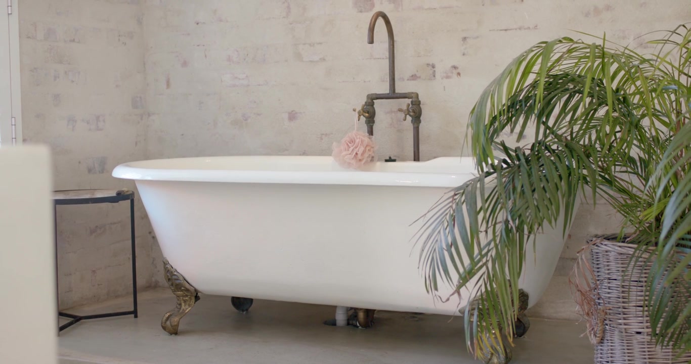 Camera is panning left, revealing tub with pouf and brass faucet showing bathroom vignette