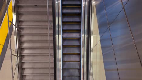 a top down interior shot, over a flight of stairs situated next to a moving escalator