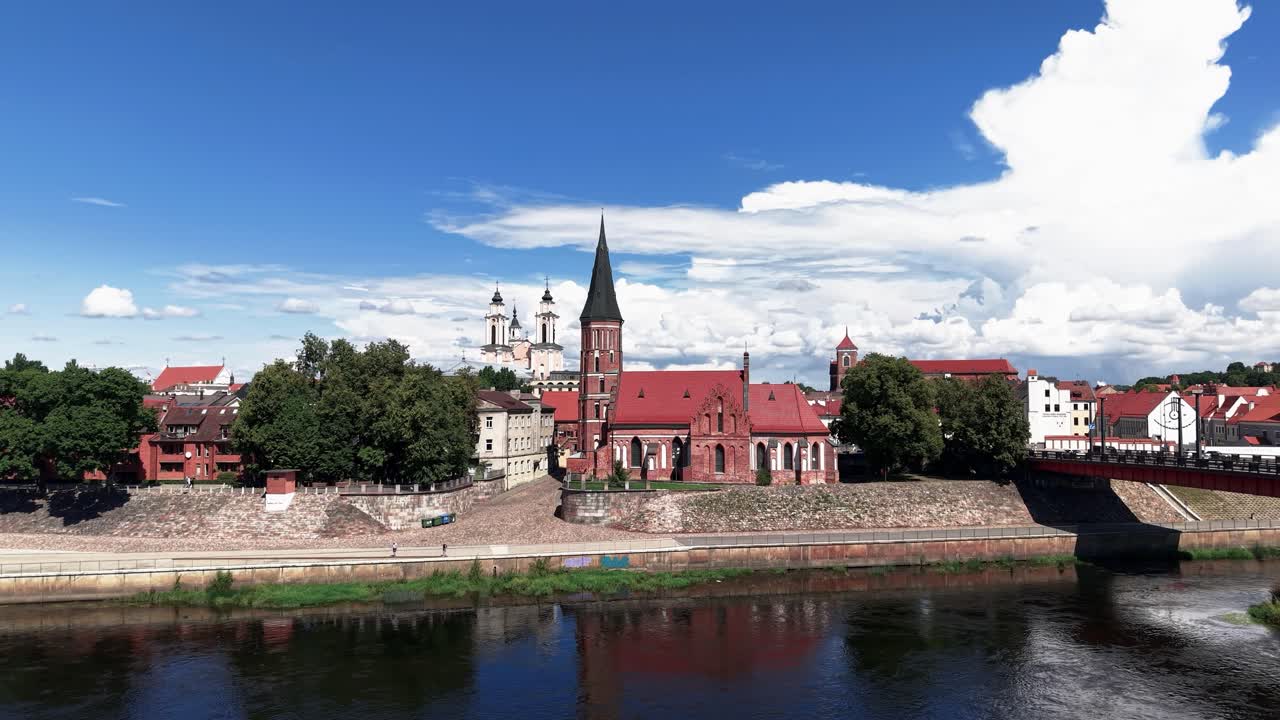 Aerial view of a picturesque European riverside town og Kaunas, Lithuania, with historic red-brick church, scenic sky, and traditional architecture reflected in calm water