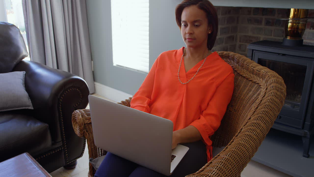 Front view of black woman working on laptop in living room at home 4k