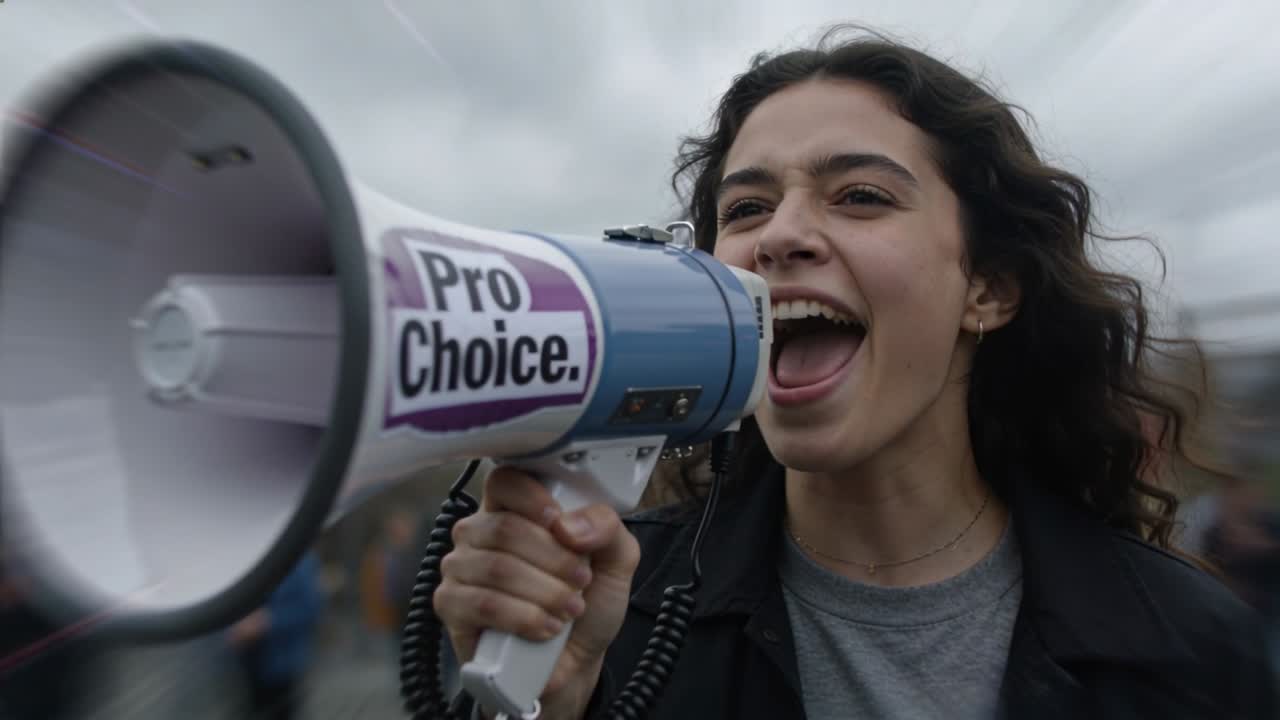 Video verticale: Urla mentre la folla canta, donna in cappotto scuro con megafono Pro Choice a un raduno