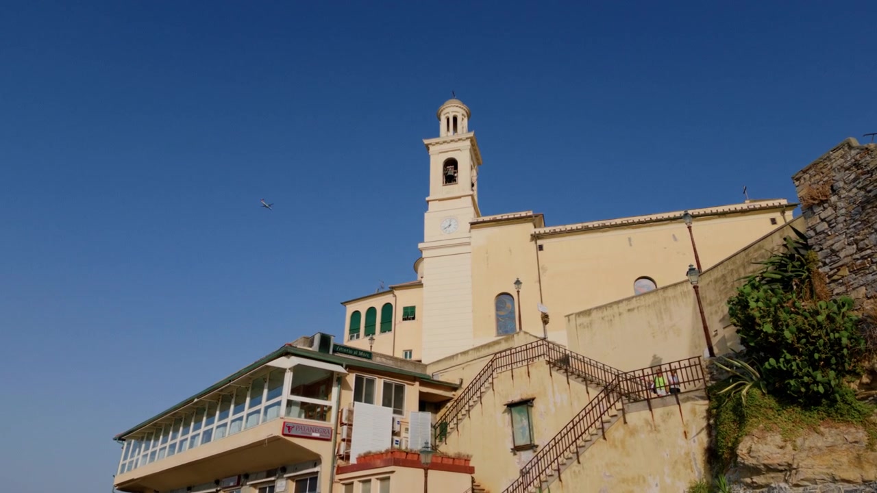 Vista dal basso verso l'alto di una chiesa storica ed edifici color pastello sotto un cielo azzurro limpido a Boccadasse.