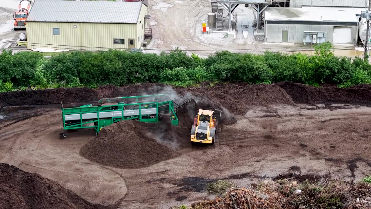 Drone view of an excavator working beside green crushing equipment inside a deep quarry pit