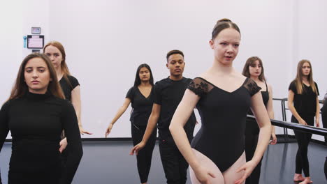 male and female students at performing arts school rehearsing ballet in dance studio using barre