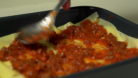 the chef is making a traditional lasagna, layering pasta sheets, meat sauce and bechamel sauce in a unique restaurant dish