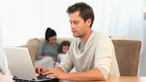 hombre trabajando en su computadora portátil mientras su familia está en el sofá