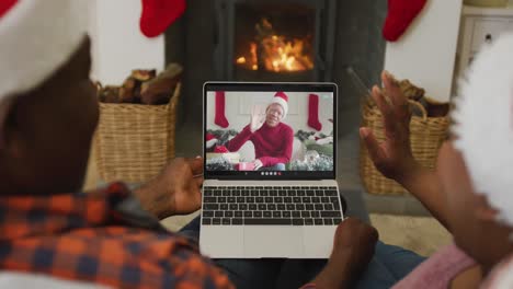 Afroamerikanisches-Paar-Mit-Weihnachtsmützen-Nutzt-Laptop-Für-Weihnachtsvideoanruf-Mit-Mann-Auf-Dem-Bildschirm
