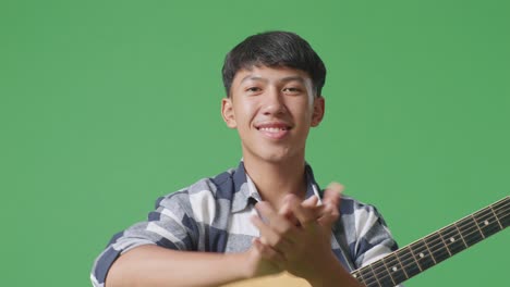 close up of asian teenager with guitar clapping his hands on green screen background