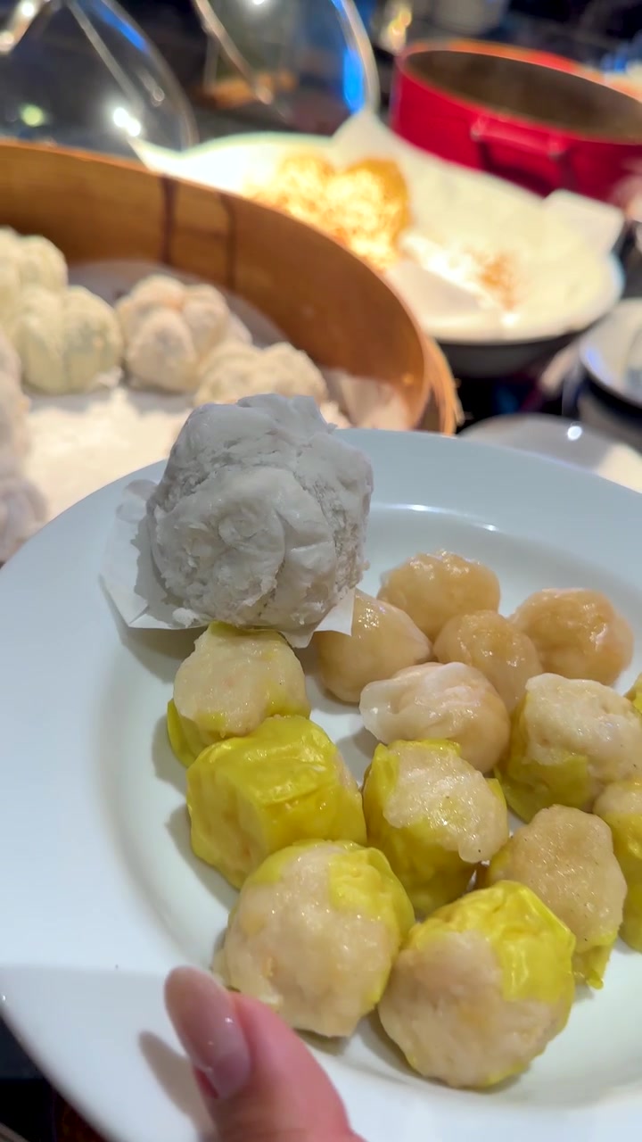 Close-up shot of tongs picking a steamed bun from a bamboo basket onto a plate