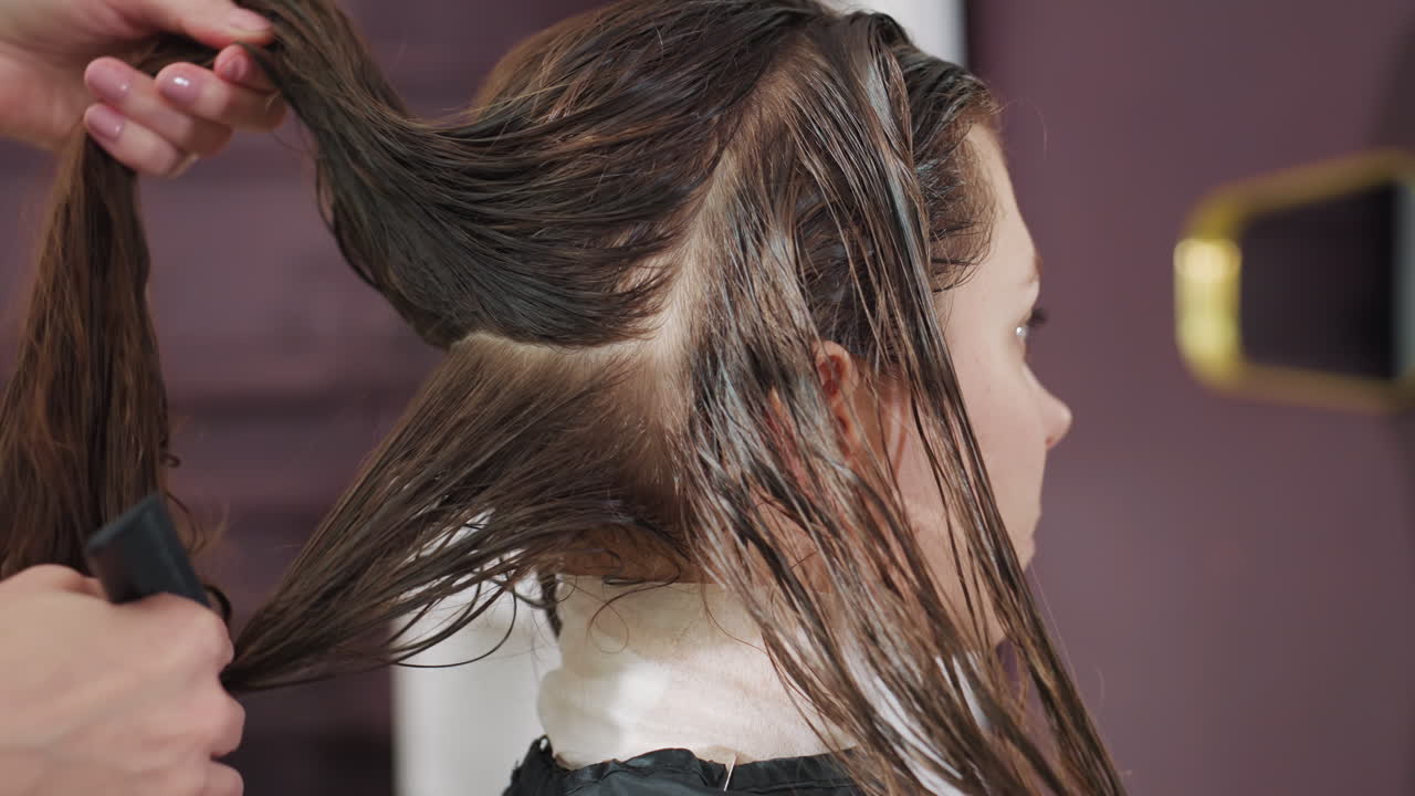 Primer plano lateral de una mujer caucásica sentada en un salón mientras el colorista peina el acondicionador sobre el cabello húmedo para una distribución uniforme, fondo suave, ambiente profesional tranquilo que enfatiza la salud del cabello.