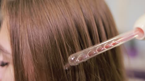 a woman is getting a hair treatment with a comb . a woman is receiving a hair treatment using a comb, a fashion accessory made of wood, enhancing her natural hair with a magenta color