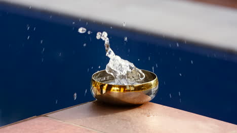 droplet falling and splashing water in a small golden bowl under daylight