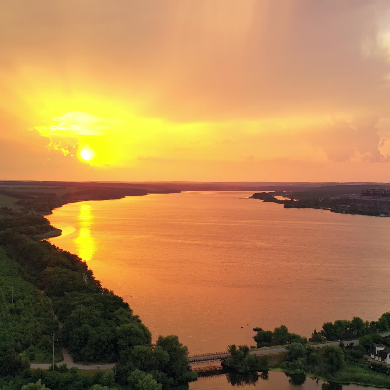 Rural background near the lake at sunset. Aerial view of pipes with smoke at the bank of the river in the evening. Amazing sunset over the beautiful scenery.