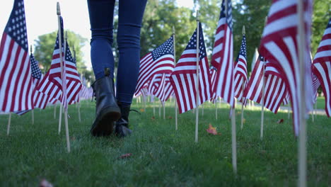 cropped image of a woman in skinny jeans and black boots walking through small american flags on grassy meadow