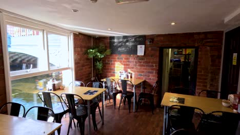 camera slowly pans across a sunlit restaurant with brick walls, wooden floors, and large windows, highlighting empty tables, chairs, and warm natural lighting