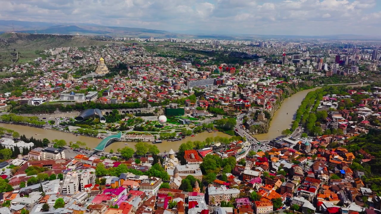 Tiflis şehir manzarasının kentsel mimariyi, kıvrımlı nehir manzaralarını ve çevredeki Kafkas tepelerini içeren sinematik drone çekimi.