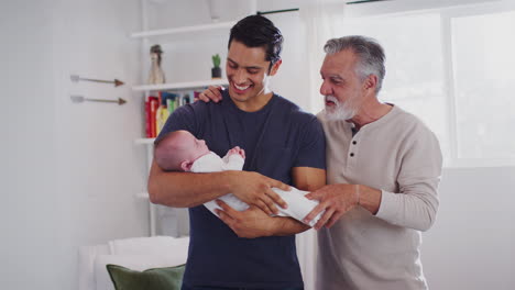 Orgulloso-Padre-Hispano-Sosteniendo-A-Su-Hijo-De-Cuatro-Meses-En-Casa,-Su-Abuelo-Parado-Junto-A-Ellos