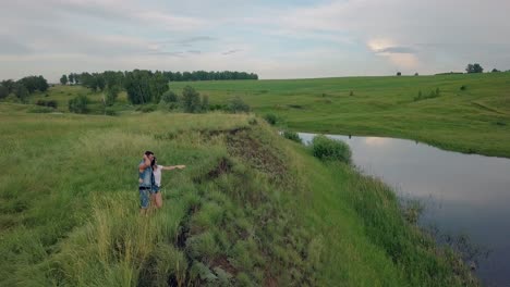 upper-view-girl-hugs-man-in-denim-vest-and-shows-blue-lake