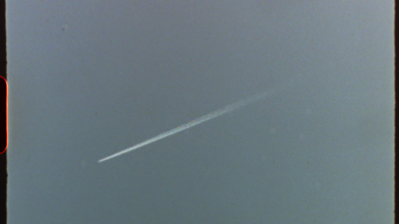 Filmed on super 8 film - white trail of an airplane flying high in the sky, with a vintage super 8 look with visible grain, scratches, and light leaks
