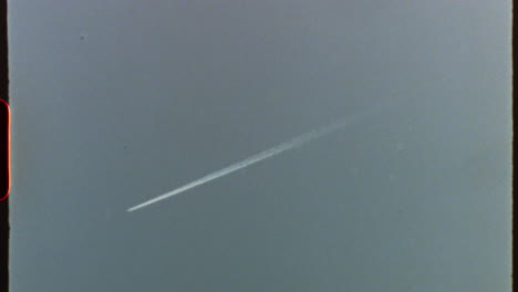 filmed on super 8 film - white trail of an airplane flying high in the sky, with a vintage super 8 look with visible grain, scratches, and light leaks