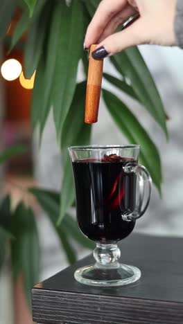 woman adding cinnamon stick to a glass of mulled wine