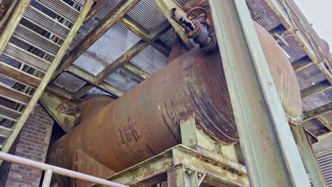gran tanque viejo y oxidado con válvula en un marco de acero