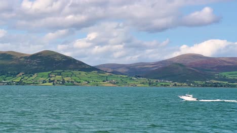 White-Speedboat-Cruising-Amidst-the-Stunning-Beauty-of-a-Sunny-Day-with-Clouds,-Framed-by-the-Majestic-Mourne-Mountains-in-Northern-Ireland