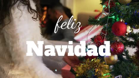 Animation-of-christmas-feliz-navidad-text-over-woman-decorating-christmas-tree