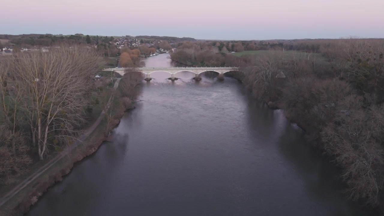 Una vista aerea al tramonto mostra un'ansa dolce del fiume con un ponte e un villaggio in lontananza lungo la Valle della Loira.