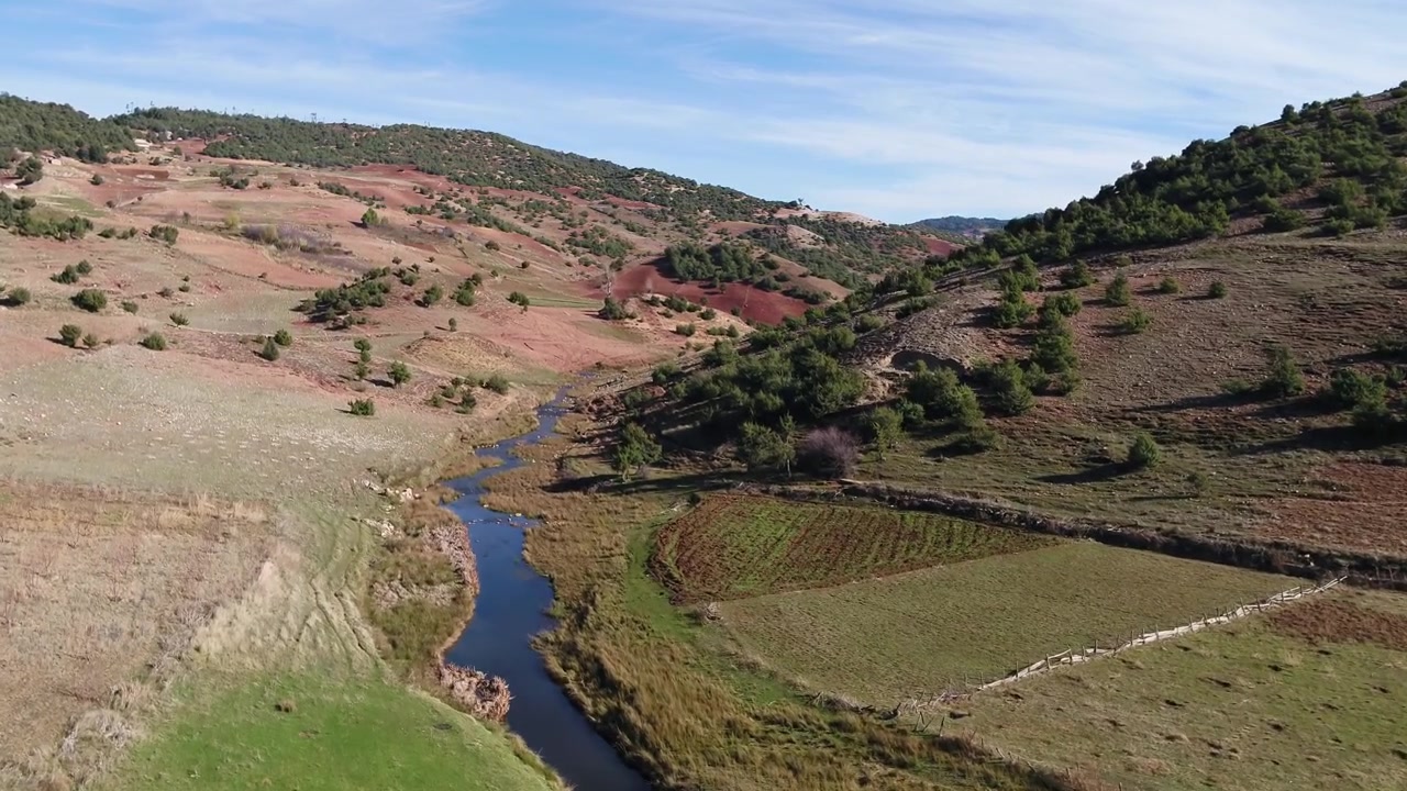Vista aerea con drone di un prato verde con un ruscello che scorre e dolci colline nel Medio Atlante, Marocco, ideale per progetti di viaggio, natura e campagna.