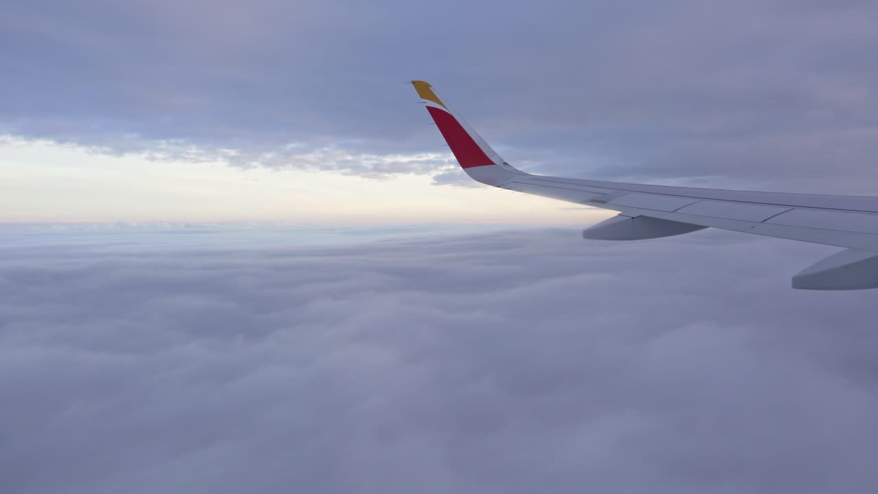 Aile d'avion volant au-dessus des nuages par une journée nuageuse, avec des nuages élevés et des nuages bas.