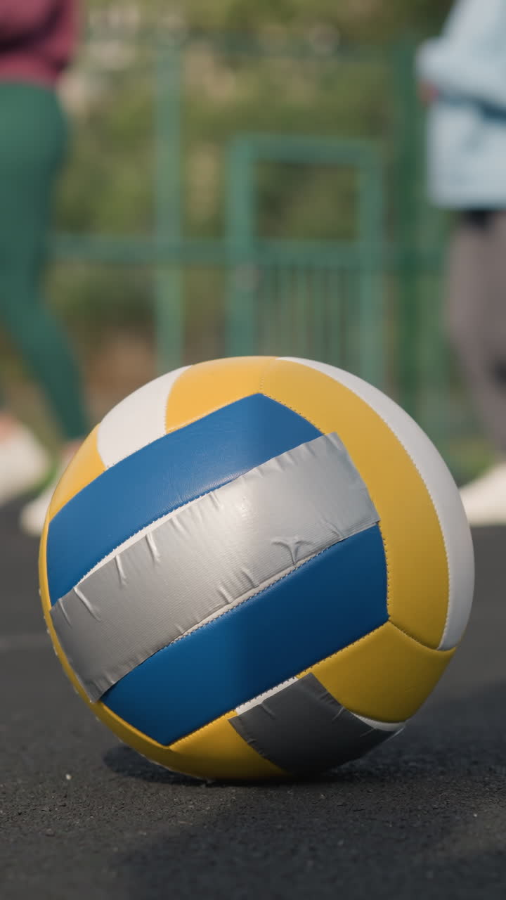 Primo piano di una palla da pallavolo a terra con sfondo sfocato, con un allenatore che guida un giovane atleta mentre fanno jogging in un campo sportivo, enfatizzando il movimento atletico e l'allenamento all'aperto