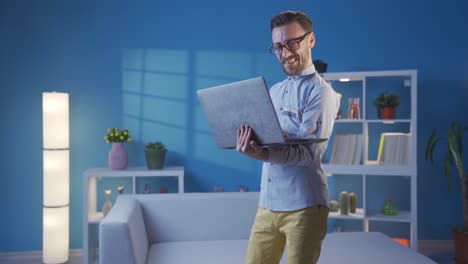 hombre de negocios guapo y carismático mirando la computadora portátil en casa y divirtiéndose mientras baila.