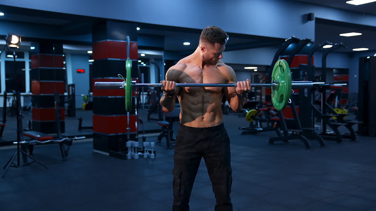 Male athlete with strong body and naked torso lifts barbell in modern gym. Slow motion.