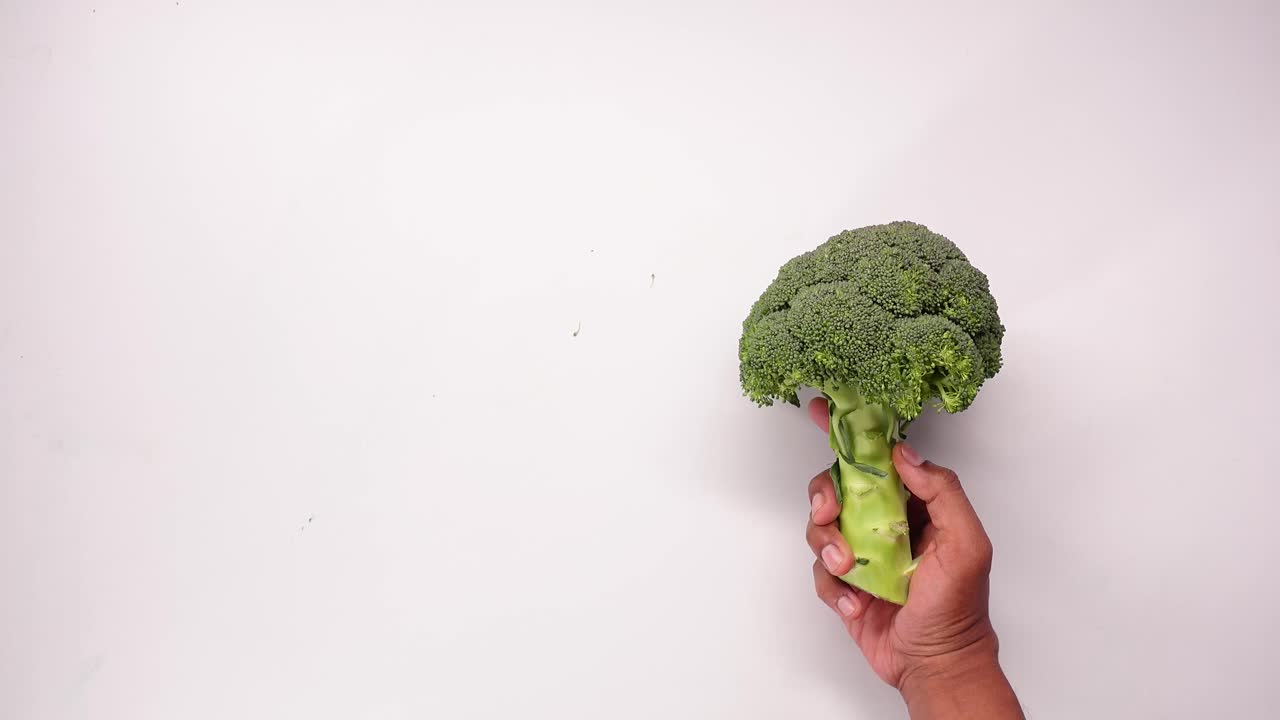 Mano che tiene broccoli freschi e verdi su sfondo bianco