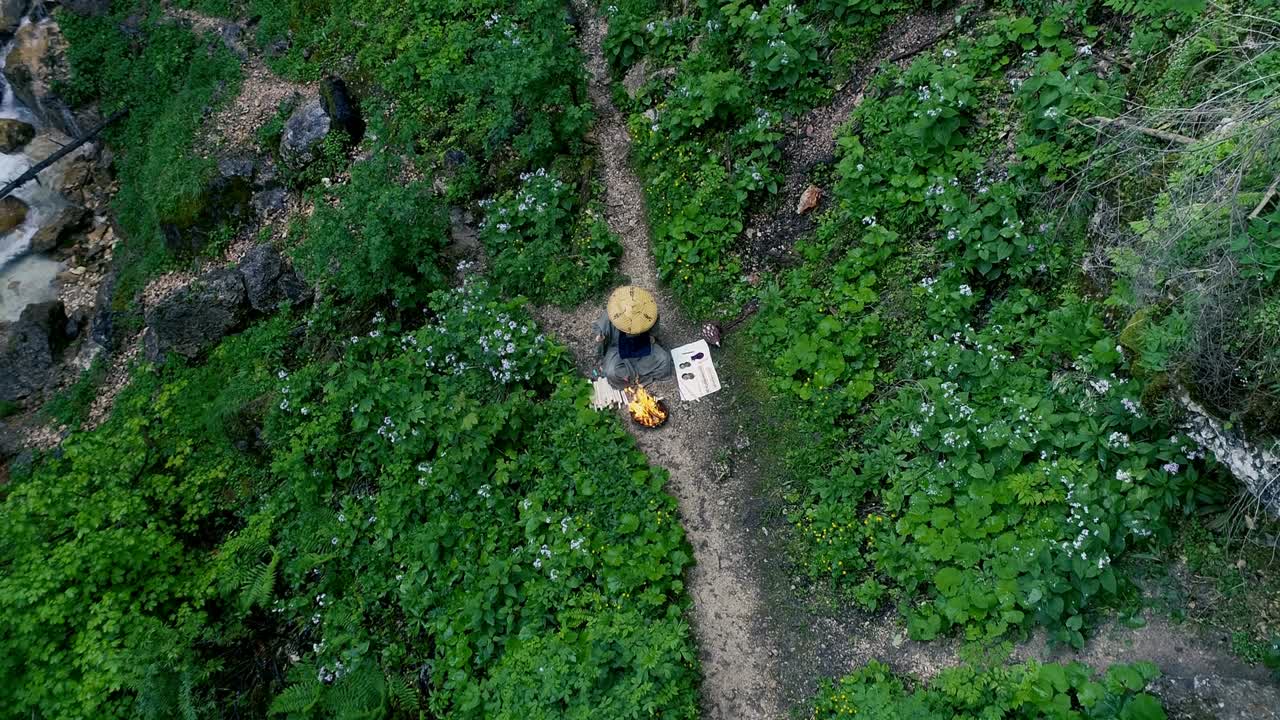 Man with beard makes fire ceremony in front of big waterfall