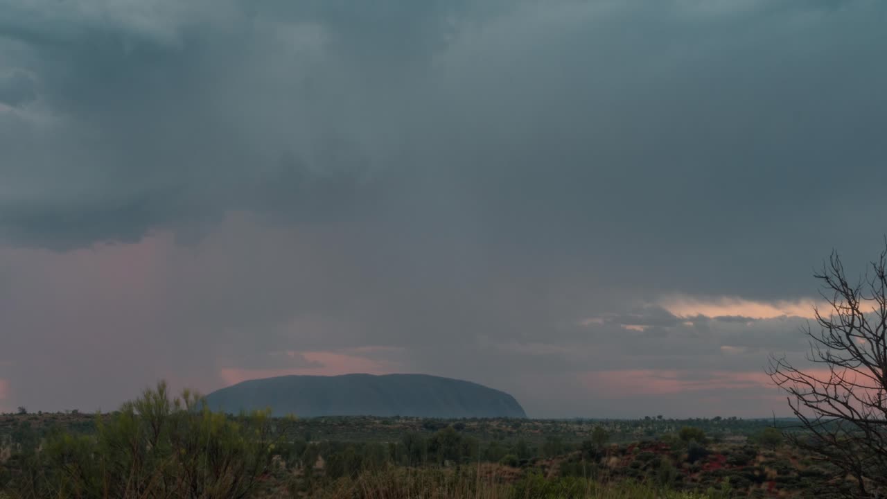 일몰 동안 호주 아웃백에서 울룰루 위로 폭풍우 구름의 시간 경과