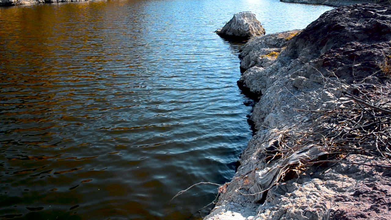 Acqua torbida che scorre placidamente sulla riva rocciosa di sabbia bianca, vista angolata dall'alto.