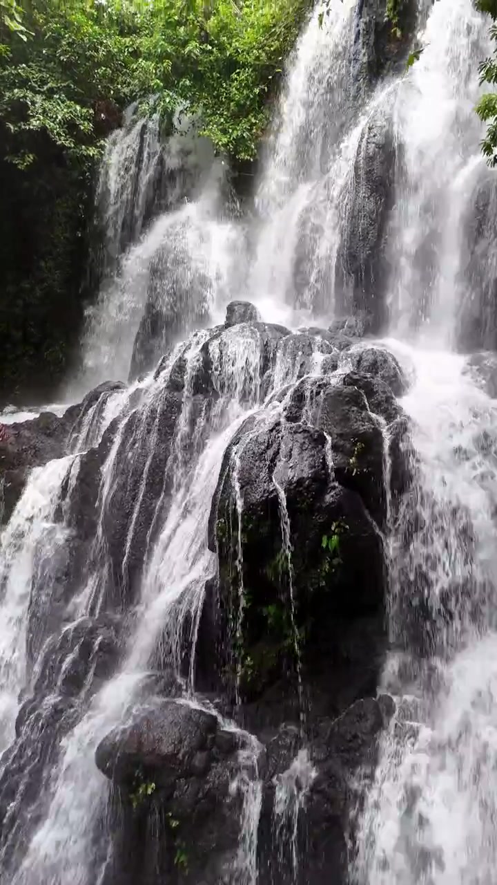 Vista aerea verticale con drone di una potente cascata a più livelli che si riversa su scuri massi vulcanici in una pozza rocciosa, incorniciata da una lussureggiante giungla tropicale, Hidden Falls, Bulusan, Sorsogon, Filippine