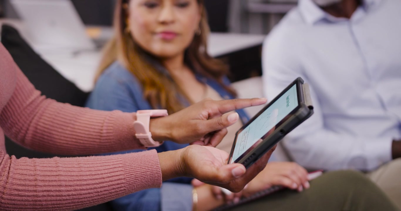 Diverse coworkers watching mature woman positioning tapping tablet showing content at meeting